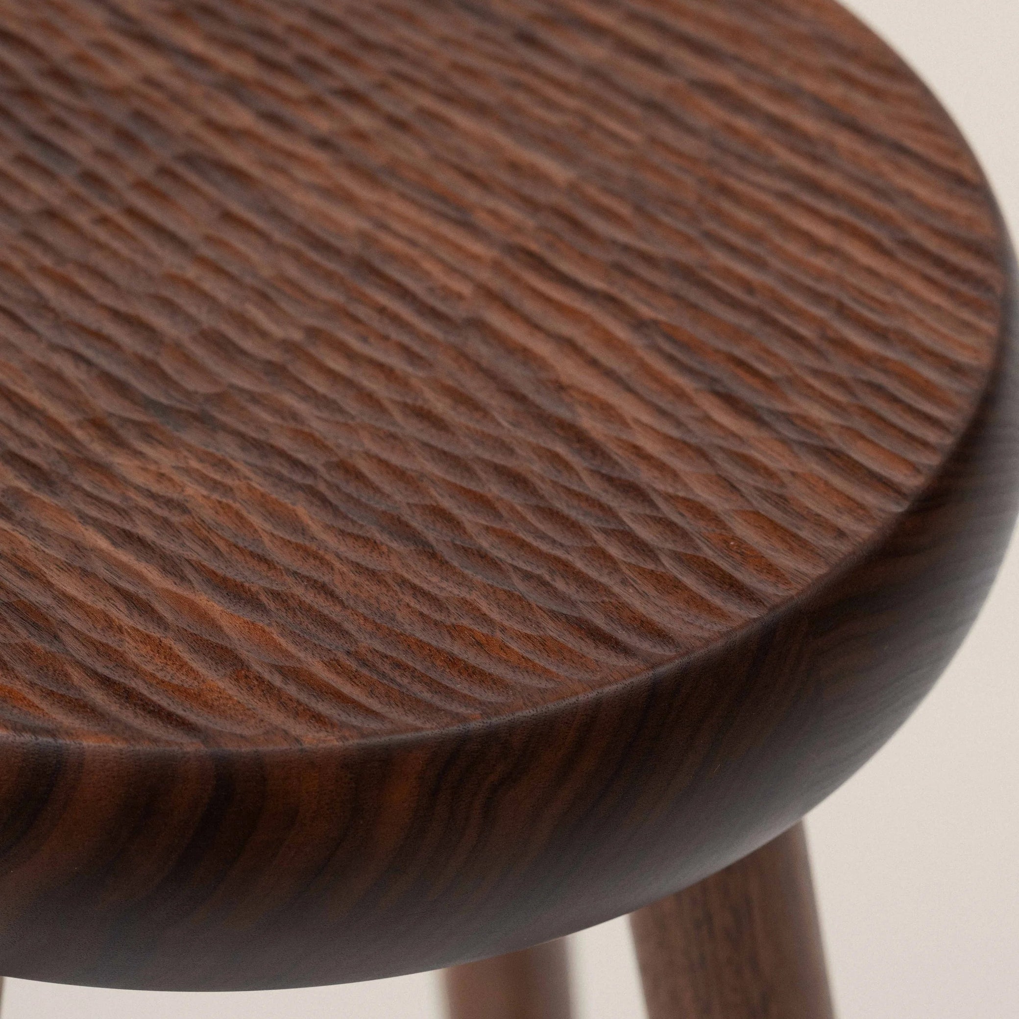 Wooden walnut stool with a round seat and four legs on a plain background