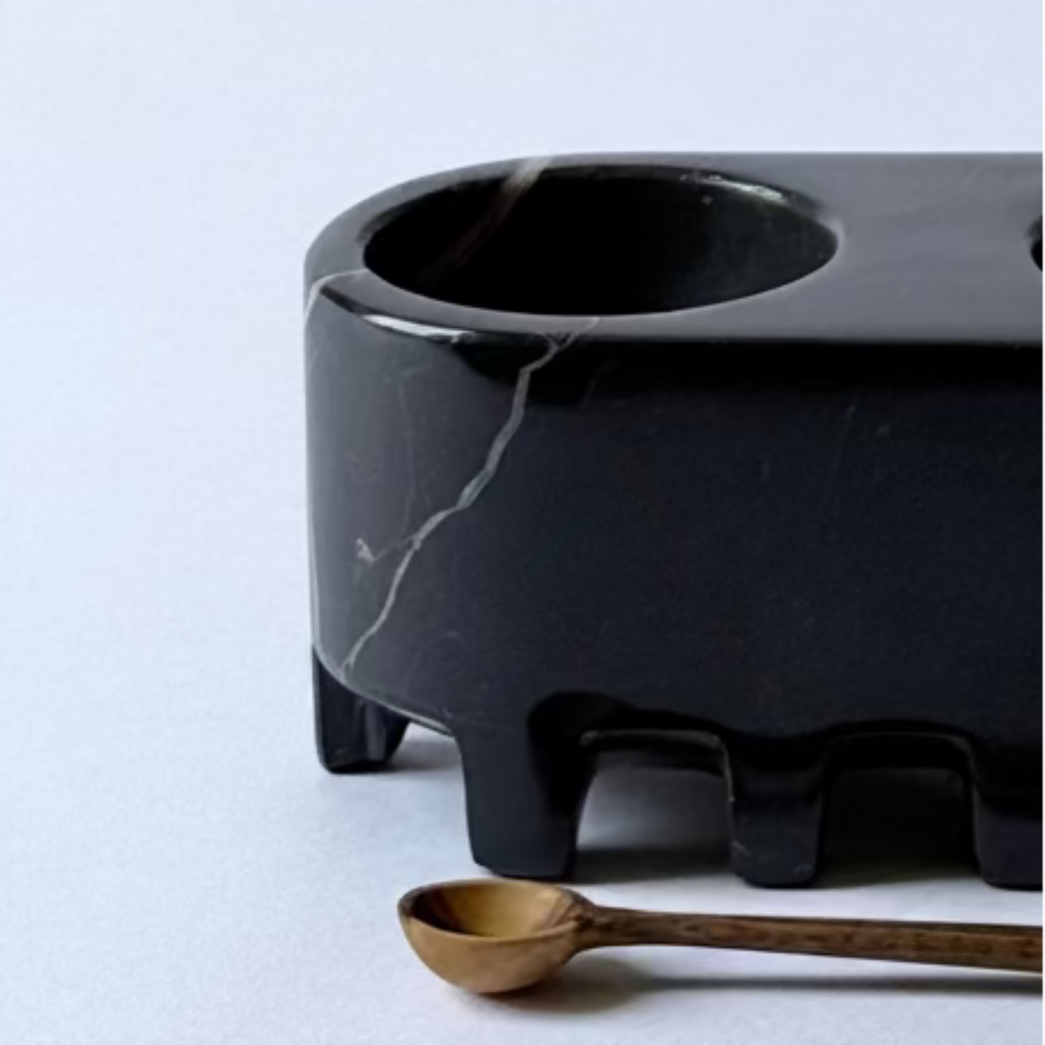 Black marble double-bowl holder with a gold spoon on a light gray background